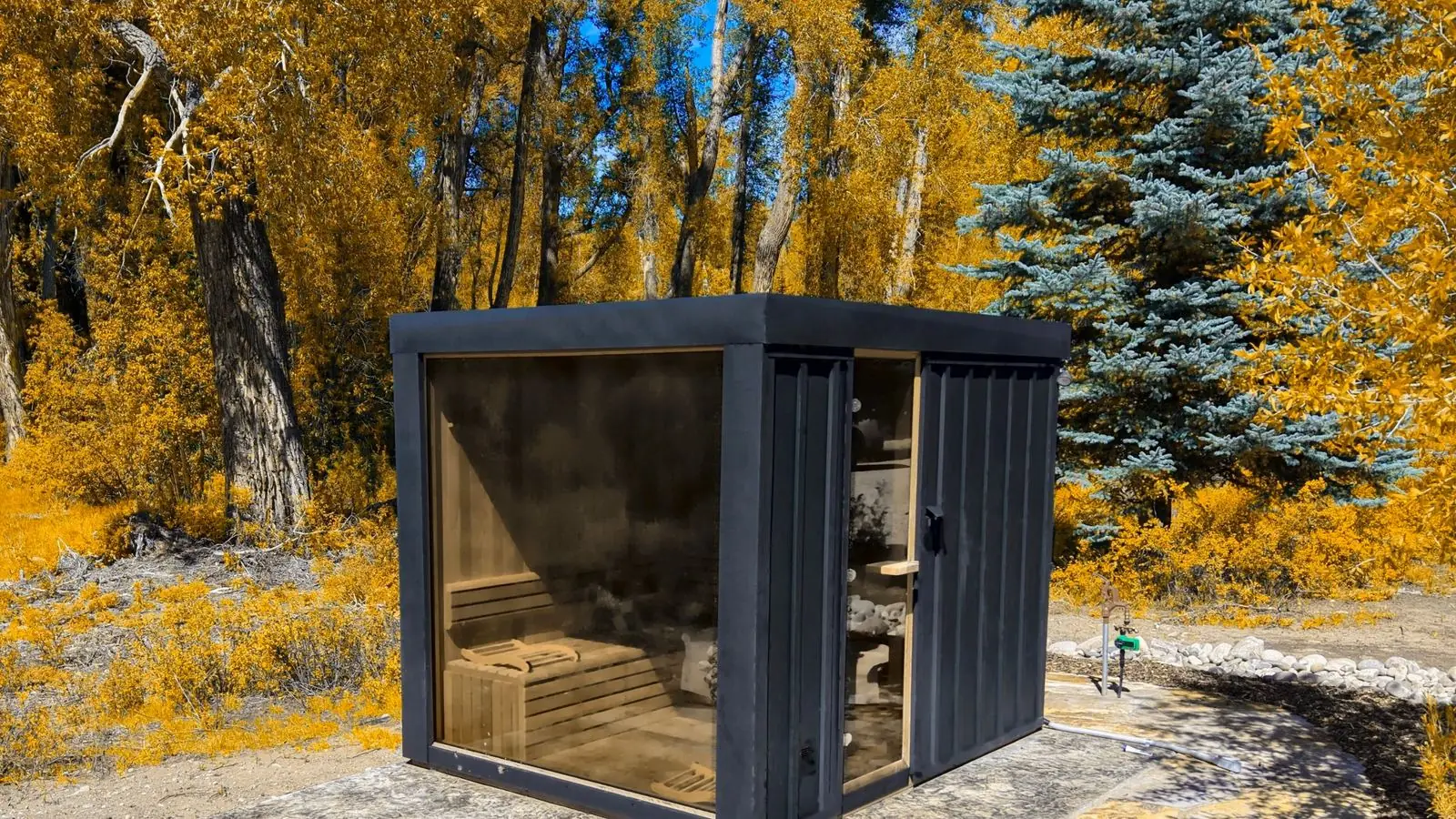 Leil Black Cube outdoor sauna on a flagstone pad, golden cottonwoods behind it