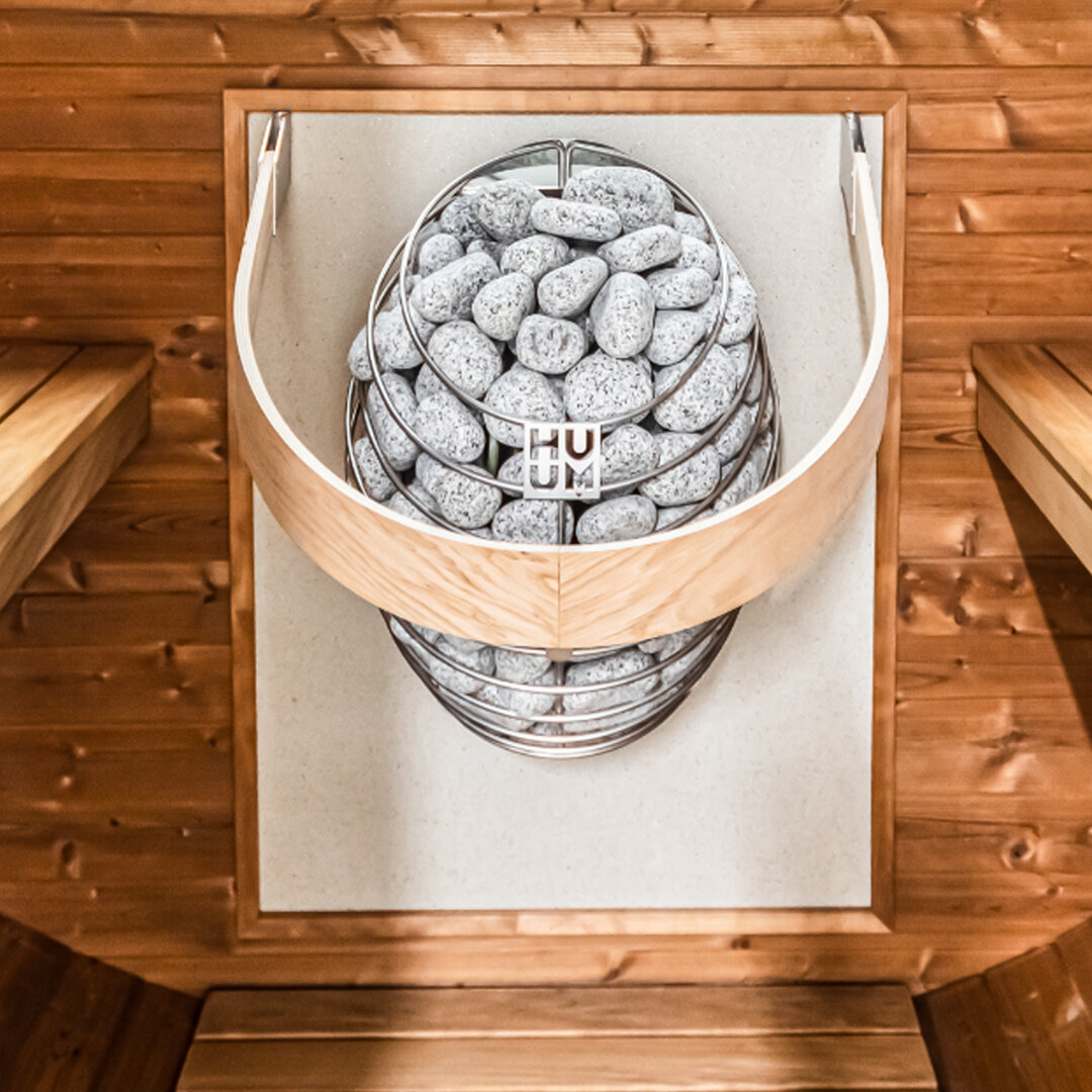 A HUUM heater filled with sauna stones inside a Thermory barrel sauna