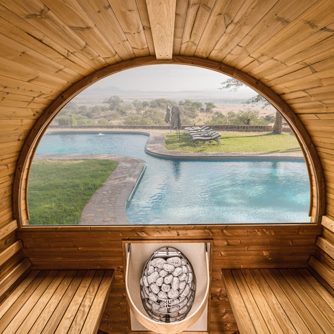 Interior of a Thermory barrel sauna looking out the panoramic half-moon window to a pool and landscape